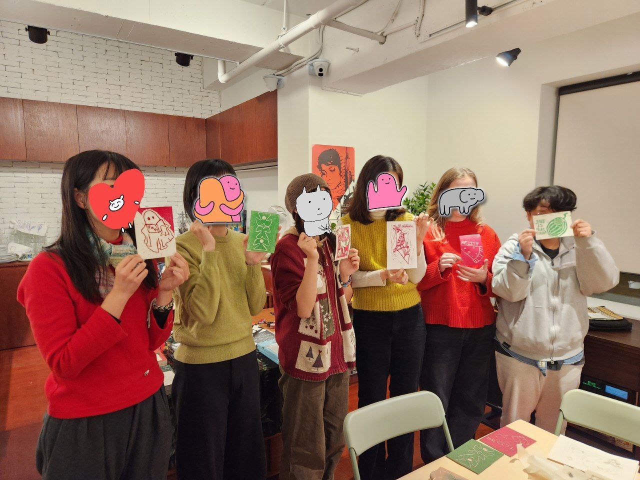 6명의 사람이 실내 공간에서 판화를 들고 나란히 서 있는 모습을 촬영한 사진이다. 각각 초록색 또는 빨간색으로 찍은 작은 판화를 들고 있으며 얼굴은 판화 또는 스티커로 가려져 있다. 