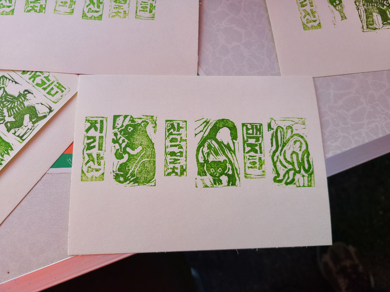 흰색 탁자 위에 초록색 스탬프가 찍힌 작은 종이들이 흩어져있다. 그 중 한 종이가 화면 가운데에 놓여있고 '지리산', '산악열차', '백지화' 라는 세로쓰기 글씨와 반달가슴곰, 담비, 토끼의 모습이 스탬프로 번갈아 찍혀있다. 