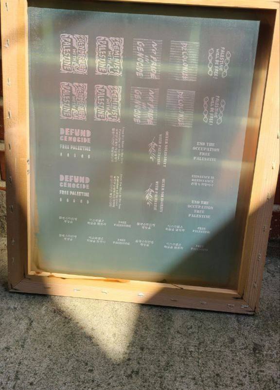 팔레스타인 해방, 핑크워싱 반대 등의 메시지를 담은 패치를 제작하기 위한 실크스크린 틀이 세워져있다. 틀 위로 햇빛이 비친다.
